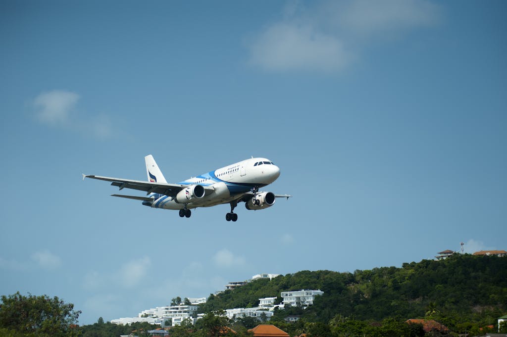 White and Blue Passenger Plane Passing Above Green Tree Covered Hill